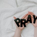 Close-up of hands holding black pray letters on white quilt background for a prayer theme.
