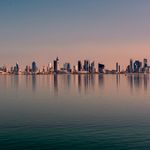 Beautiful Kuwait City skyline reflected on calm water at sunset, showcasing modern architecture.