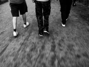 Black and white image capturing three people walking with motion blur effect.